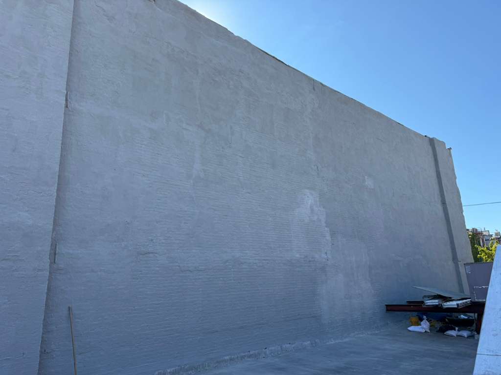 Completed exterior wall waterproofing with a uniform light grey cementitious coating