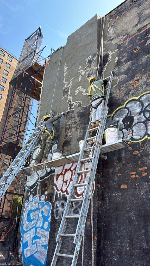 Worker hand-troweling a cementitious waterproof coating onto a repaired brick wall